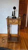 Wooden side table with drawer, black rotary candlestick phone on top.