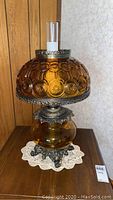 Full view of amber colored glass table lamp with brass base and amber hurricane shade showing its round ornate design and height.