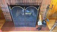 Front view of fireplace screen with tools and holder, fireplace grate visible inside fireplace.