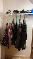 Three vintage military jackets hanging on wire shelf with insignia patches visible on sleeves, two US flags and uniform hat above.