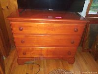 Front view of a wooden chest of drawers showing three drawers with round wooden knobs, medium wood tone, some surface scratches and nicks visible.
