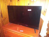 Front view of the Sansui LED TV placed on wooden furniture against wooden wall.