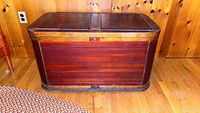 Front view of vintage cedar chest with reddish wood panels, metal bottom trim and a lock in the center.