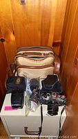 Contents displayed on small cabinet: Canon camera with lens, second lens in plastic bag, Vivitar flash in pouch and beige camera bag behind