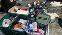 Overview of storage bins containing holiday decorations including Caroler figurines, slate art, serving pieces, and lights.