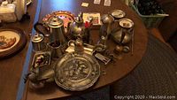 Photo of assorted pewter and metal tea and coffee pots, crumb saver dish, bells, candle snuffer, and other metalware on a wooden table.