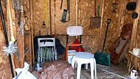Wide view inside shed showing convertible hand truck, various yard tools and plastic stools.