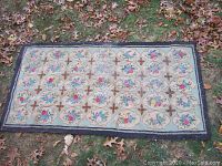 Full image of the antique oriental wool rug laid out on grass with autumn leaves. Shows overall design and color scheme.