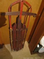 Top side view of the antique Western Clipper childs sled showing wooden slats and red metal supports.
