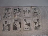 Photo showing 8 black and white vintage baseball cards laid out on light surface, each card featuring a player posing with a bat or in fielding stance, signatures visible on front