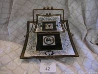 Two-tiered serving tray with decorated square glass plates and brass frame, displayed folded for transport.