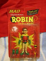 Front view of MAD Alfred E. Neuman as Robin The Boy Wonder action figure sealed in blister pack with visible accessories inside.