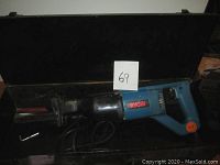 Full view of the reciprocating saw inside the metal carry case with visible RYOBI logo, electrical cord, and blade attached.