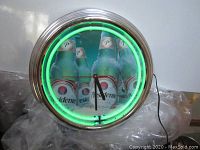 Front view of the round neon wall clock showing green neon light and El Presidente beer bottles advertising on the clock face.