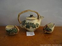 Front view of 4-piece vintage McCOY tea set on wooden surface showing teapot, sugar bowl, and creamer with ivory base and green ivy decoration