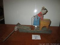 Side view of wooden whirligig showing the woman in blue skirt and red top bending over the wash tub with a propeller blade at back.