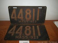 Two matching vintage Massachusetts porcelain license plates from 1923 with number 44811, showing their age and patina on a wooden surface.