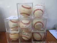 Photo shows eight autographed Major League baseballs in display cases and plastic bags arranged in a pyramid. Signatures include Mickey Pina, Frank Viola, Jeff Reardon, Tom Brunanski, Scott Fletcher (labeled), Jody Reed, Al Hrabosky, and one unknown.