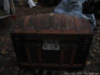 Closed dome top steamer trunk showing curved lid with wood straps and stamped tin exterior.