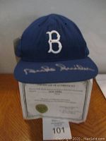 Front view of blue Brooklyn Dodgers baseball cap with white 'B' and Duke Snyder autograph on brim, Certificate of Authenticity visible underneath.