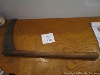 Top view of antique wooden handled scythe with serrated metal blade laid on patterned wood table.