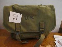 Front view of olive drab canvas utility bag with 'U.S.' marked on the flap and two adjustable canvas straps with metal buckles.