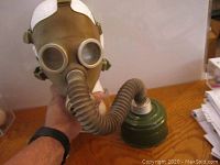 Front view of the gas mask attached to a mannequin head showing the hose and canister placed on the wooden surface.