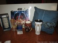 Photo shows Star Wars collectible set including Stormtrooper liquor glass, Lando design drinking glass and travel mug, vintage Tusken Raider mug, Death Star ice tray, vintage Star Wars pillow, and Star Wars calendar.