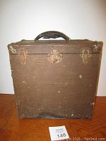 Front view of the antique leather covered wood music box case showing metal clasps, handle, and visible wear marks