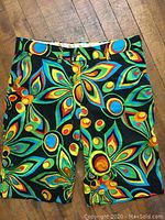 Front view of men's LoudMouth shorts in size 34 showing bright abstract colorful floral and circular pattern on black fabric with button and zipper fly.