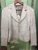 Front view of light cream women's jacket with floral brocade pattern on hanger