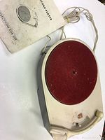 Top view photo of the toy record player showing red felt turntable, tonearm, and attached power cord. Accompanied by the instruction manual.