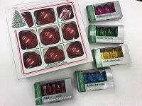Smaller boxes of Alderbrook indoor decorative bulbs in purple, green, yellow, red, and blue colors stacked next to the box of red glass ornaments.
