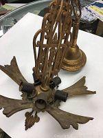 Photo showing the overall antique Art Deco ceiling light fixture with 5 light sockets, intricate metalwork with scroll and geometric designs, and a gold-tone finish.