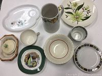 Photo showing the ten vintage dishes arranged including the pitcher, plates, bowls, and covered dish with various floral and geometric patterns.