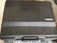 Black textured carrying case with handle, closed, showing the Smith Corona badge on top