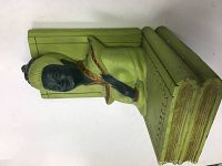 Full side view of vintage chalkware bookend featuring bust of a man in green clothing and black painted face and hands, mounted on green backplate designed for bookend use.