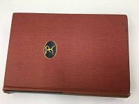 Top view of closed red hardcover book with a black and gold emblem in the center and some wear on edges.