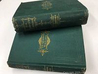 Two antique hardcover books with green covers stacked, showing gold embossed title 'De Quincey's Writings' on front and spine