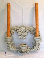 Front view of ornate plaster cement triple candle holder with two orange taper candles inserted.