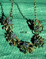 Image showing the full 16 inch vintage necklace with blue rhinestone clusters and gold-tone leaf motifs on green background.