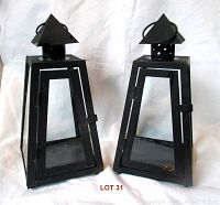 Pair of black metal lanterns with trapezoidal shape and glass panels on white background.