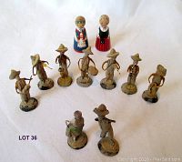 Full spread of all 12 miniature figures arranged on a white background showing musicians in hats and two female dancers in colorful traditional dresses.