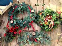 Overview of two large decorated artificial Christmas wreaths, one greenery swag, and a bunch of artificial red berries on a wooden surface.