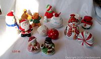 Twelve ceramic Christmas-themed salt and pepper shakers arranged on white background, featuring Santa Claus, snowmen, teddy bears, ornaments, and holiday characters.