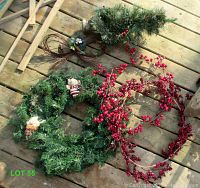 Photo showing three artificial wreaths laid on wooden floor, including berry decorated grapevine wreath and green wreaths with small decorations.