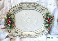 Full view of large oval ceramic serving platter with holly and berry decorations on handles, placed on lace cloth background.