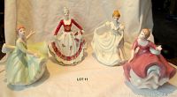 All four vintage porcelain lady statues together on beige cloth background showing different gown colors and poses
