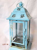 Front view of the pale blue metal lantern candle holder with glass door and floral cutouts.