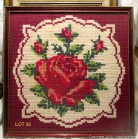 Full view of framed needlepoint showing single large red rose with smaller buds and green leaves, enclosed in a wooden frame with glass.